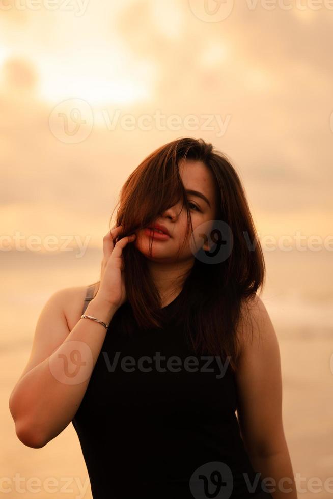 un asiatique adolescent relaxant sur le plage portant noir vêtements et posant magnifiquement photo