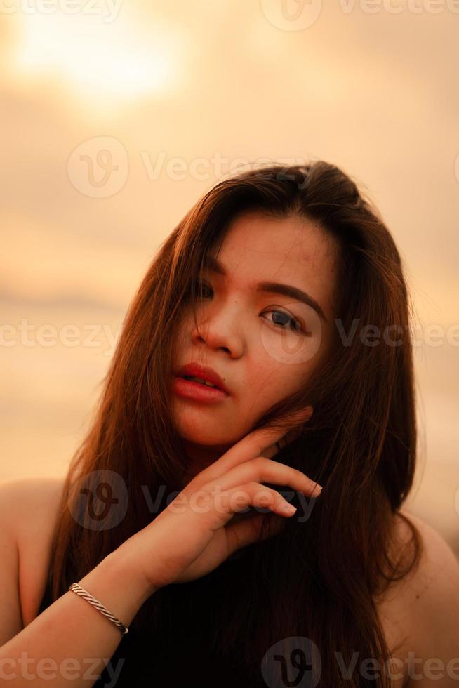 une magnifique et sexy asiatique femme avec plat faciale expressions et posant avec le sien main en dessous de le sien menton photo