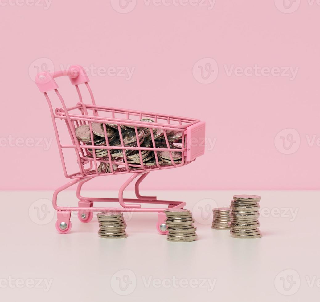 panier miniature en métal et une pile de pièces sur un tableau blanc. le concept de remises et de ventes, les économies budgétaires. commerce en ligne photo