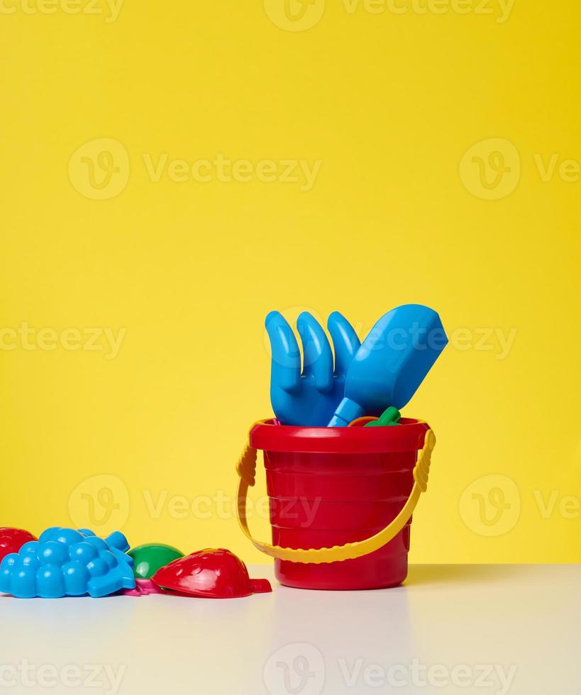 bébé rouge Plastique seau avec pelle et jouets sur une Jaune Contexte photo