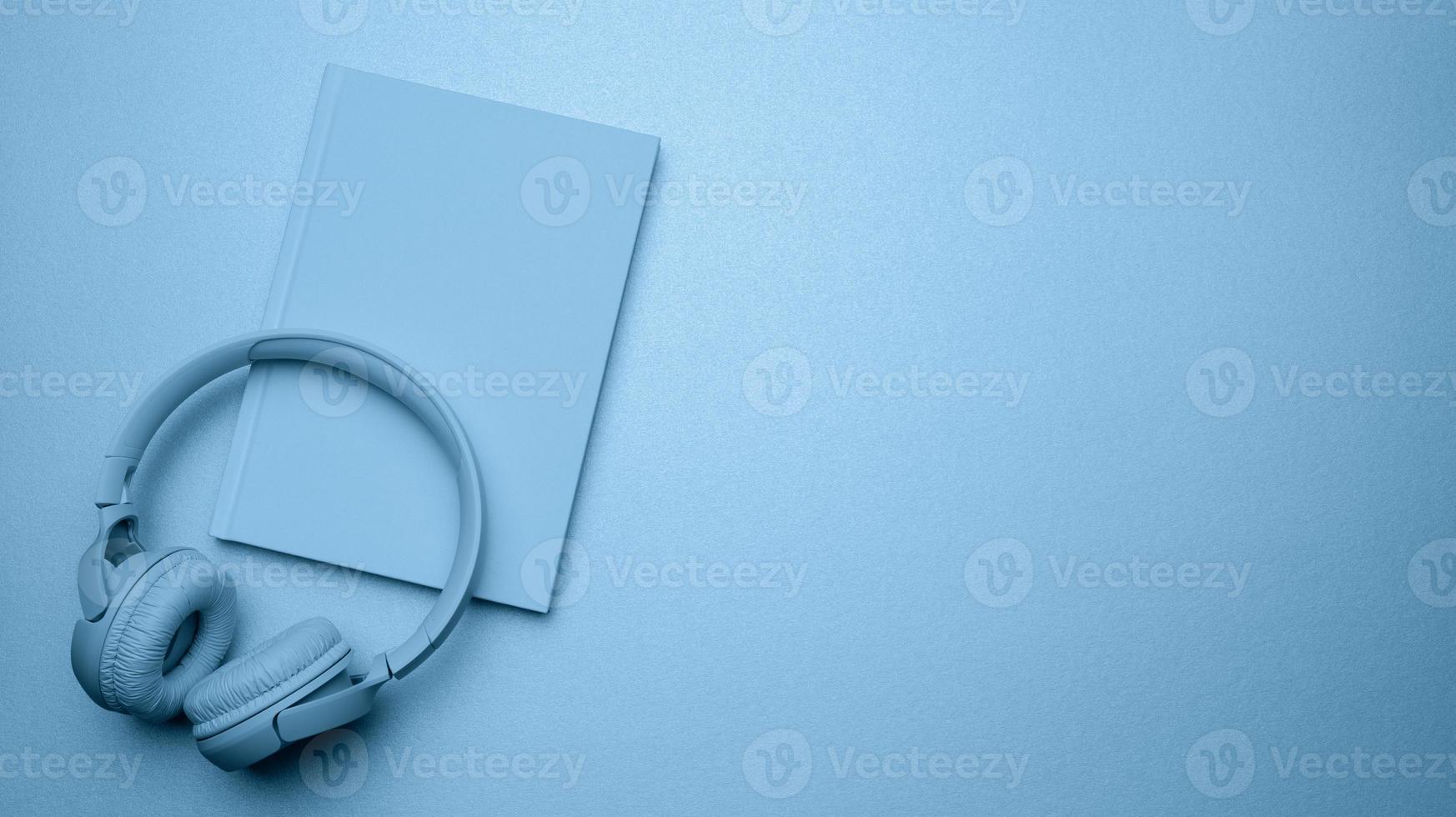 bleu sans fil écouteurs et une fermé bloc-notes sur une bleu Contexte. photo