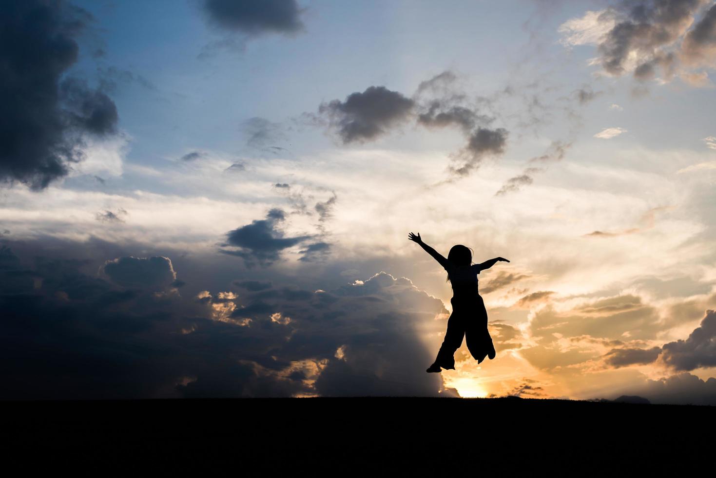 silhouette de femme heureuse sautant au coucher du soleil photo