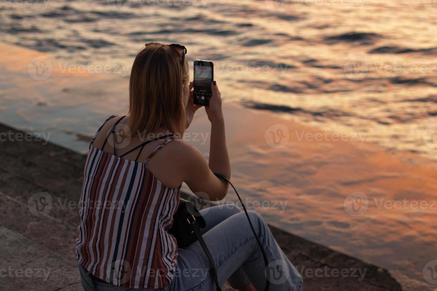 fille touristique photographies sur le téléphone une magnifique l'eau paysage à le coucher du soleil photo