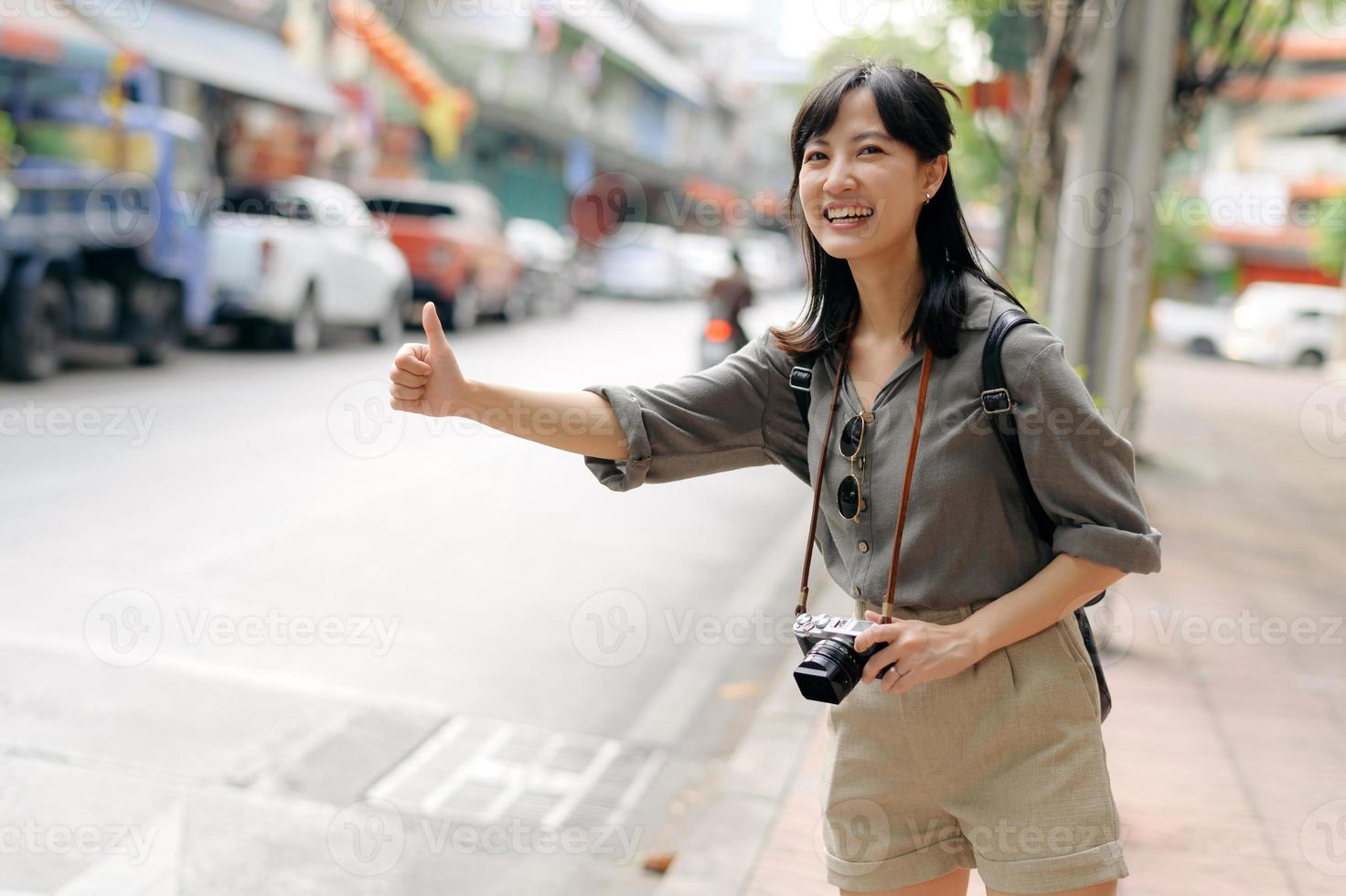 souriant Jeune asiatique femme voyageur auto-stop sur une route dans le ville. la vie est une périple concept. photo