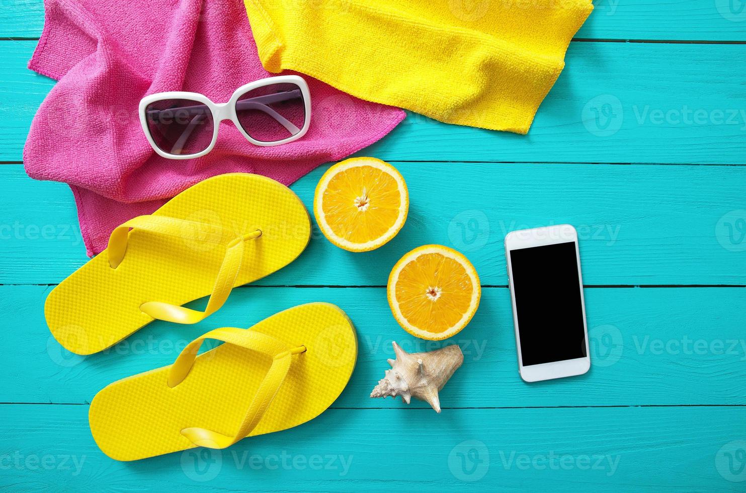 été accessoires sur bleu en bois Contexte. Jaune retourner flops, les serviettes, des lunettes de soleil, mobile téléphone et des oranges. moquer en haut et Haut vue photo