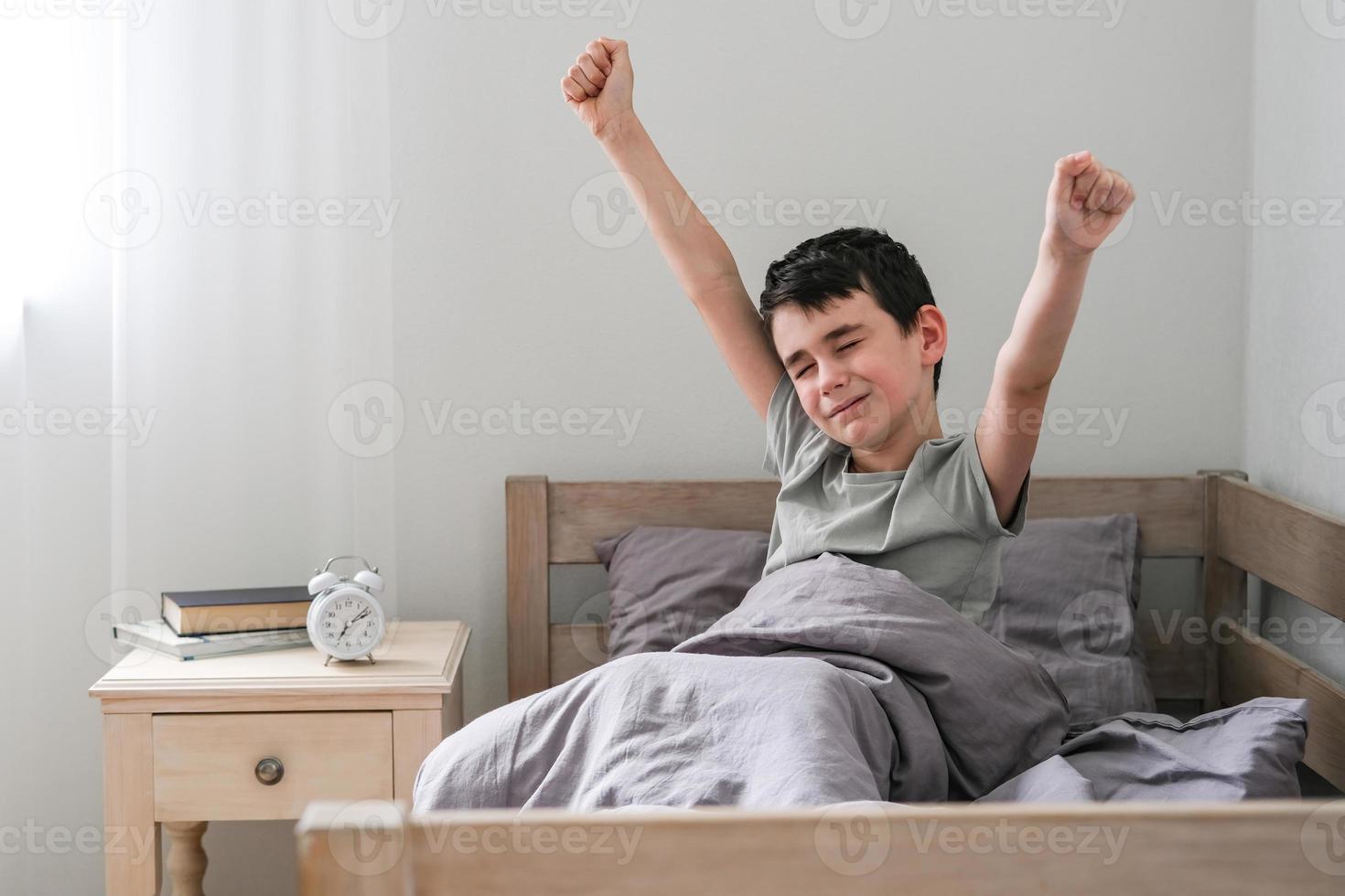 de bonne humeur garçon s'étire après veille en haut dans lit. Matin de le écolier photo