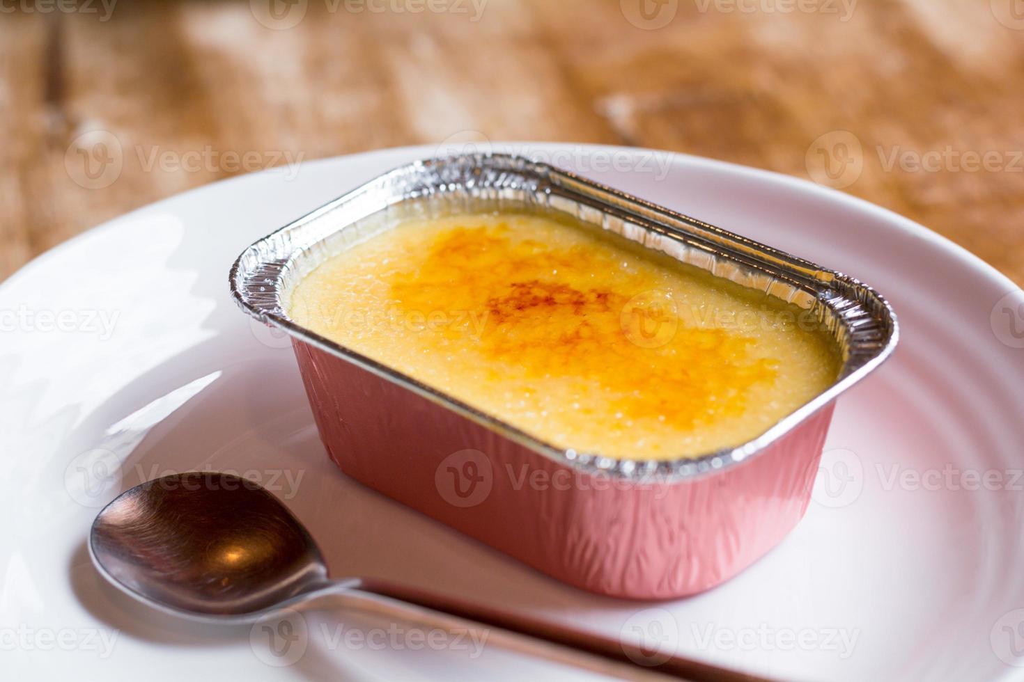 français crème brulée dans une déjouer tasse sur le blanc plaque, avec le cuillère sur le côté. photo