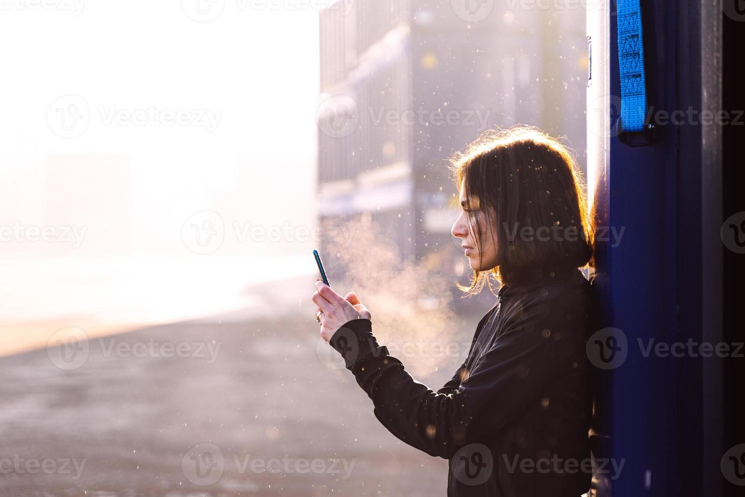 Jeune adulte femelle coureur est en utilisant téléphone intelligent parmi le conteneurs de une commercial Port photo