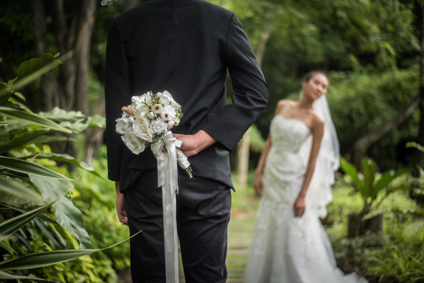 Portrait d'un marié cachant un bouquet floral derrière son dos pour surprendre la mariée photo