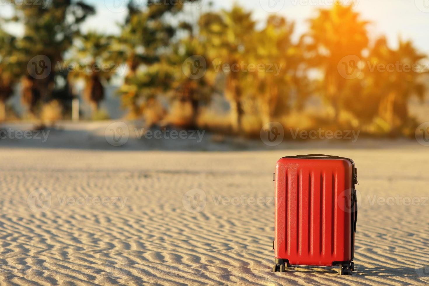 été Voyage et touristique Planification vacances. rouge valise dans le magnifique le sable plage sur paumes des arbres et sunlights Contexte. de bonne heure réservation pour été vacances. endroit pour texte photo