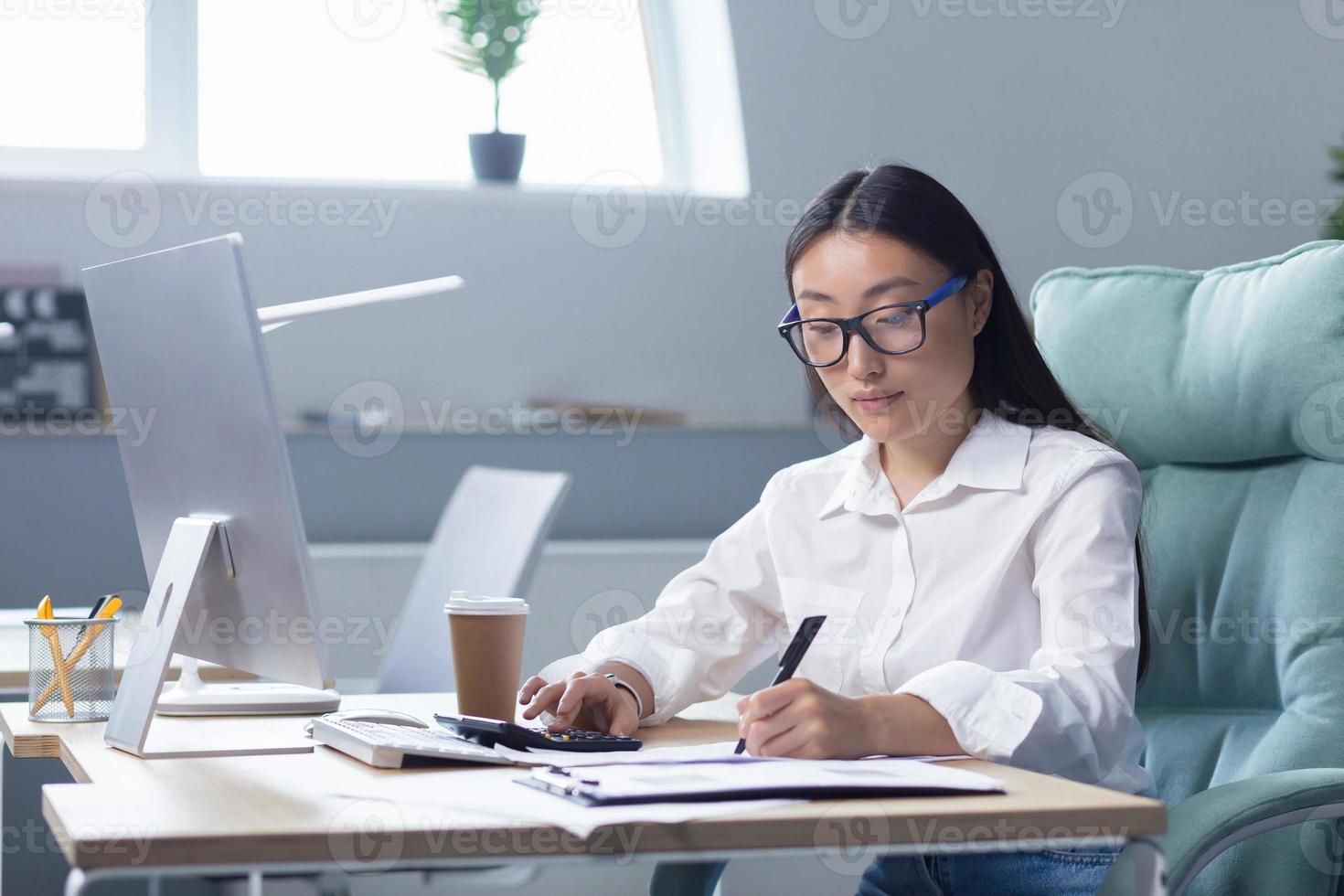 bourreau de travail. un asiatique affaires femme séance à le table en buvant café à aller dans Bureau photo
