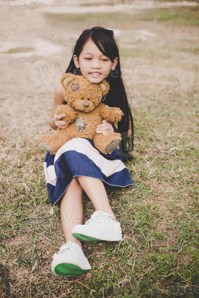 jolie fille asiatique avec ours en peluche assis dans un champ photo