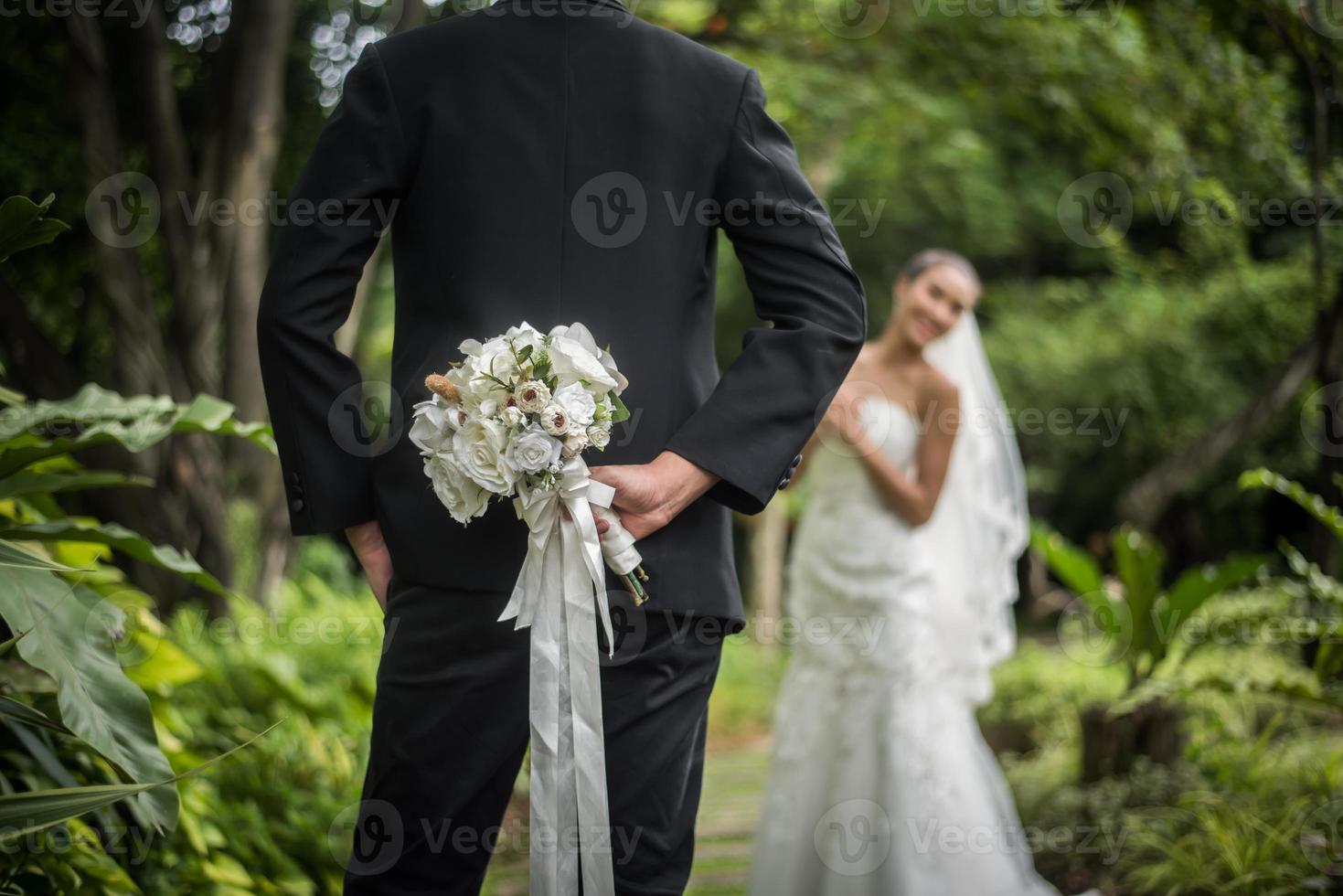 Portrait d'un marié cachant un bouquet de fleurs derrière son dos pour surprendre la mariée photo