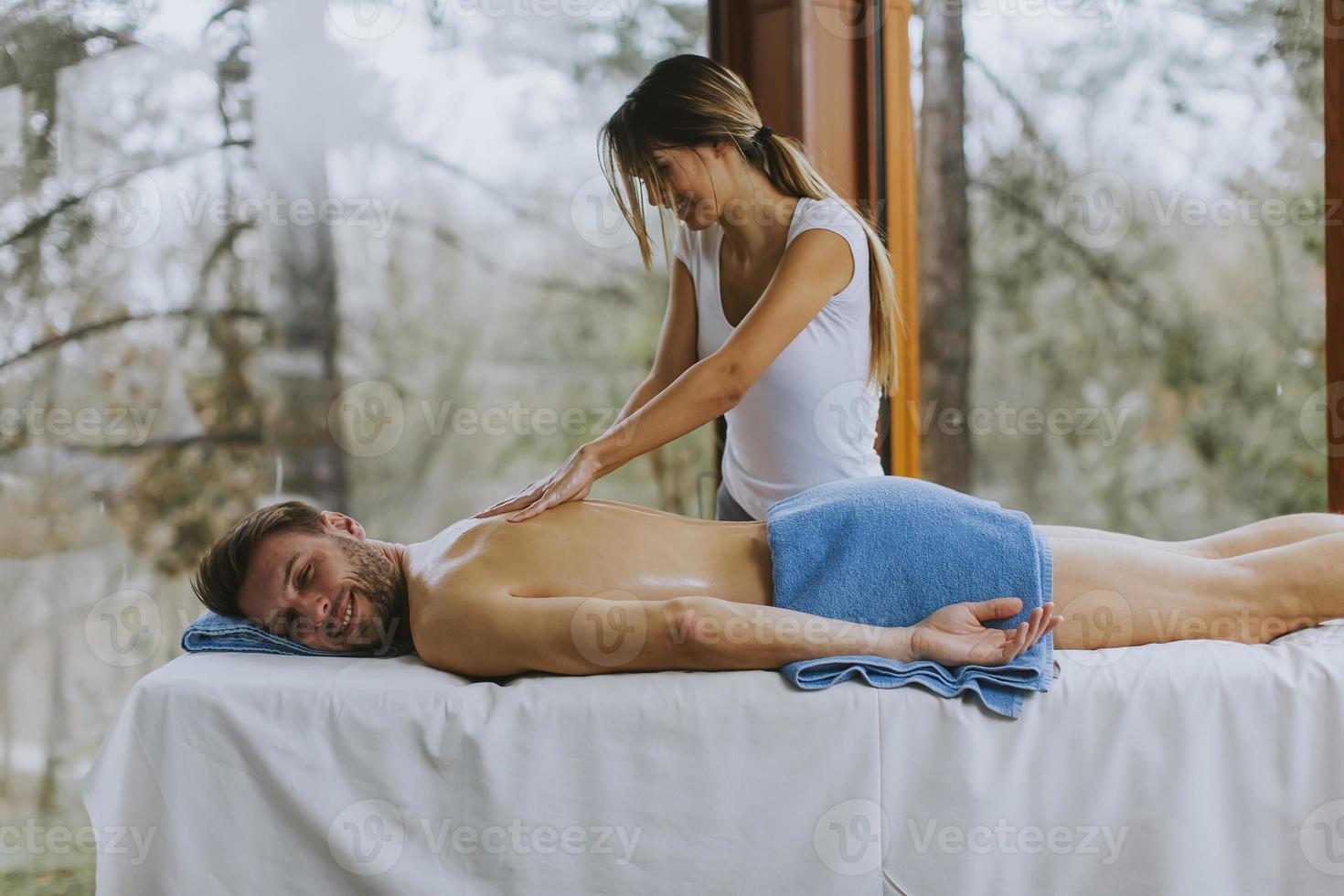 Beau jeune homme couché et ayant un massage du dos dans un salon de spa pendant la saison d'hiver photo