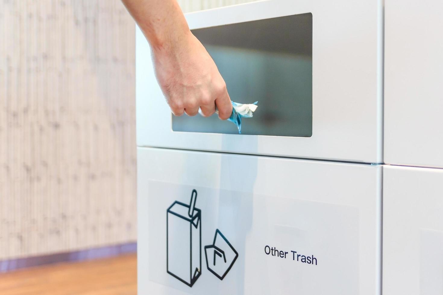 Jeune homme mettant un sac en plastique dans un bac de recyclage à l'aéroport photo