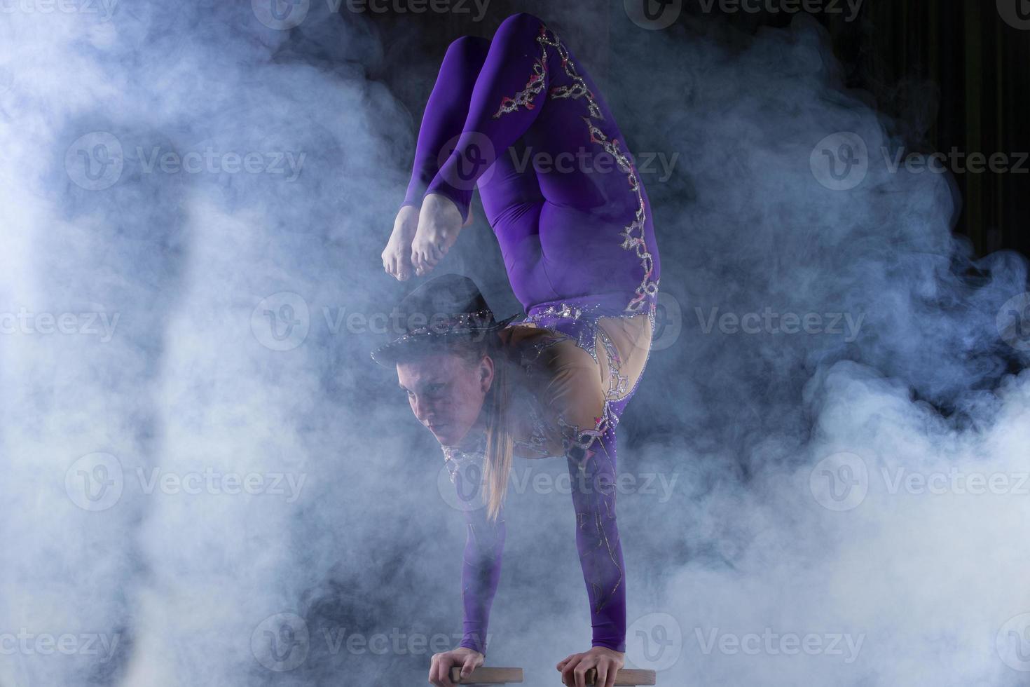 un acrobate fille effectue une magnifique cirque tour dans bouffées de violet fumée. photo