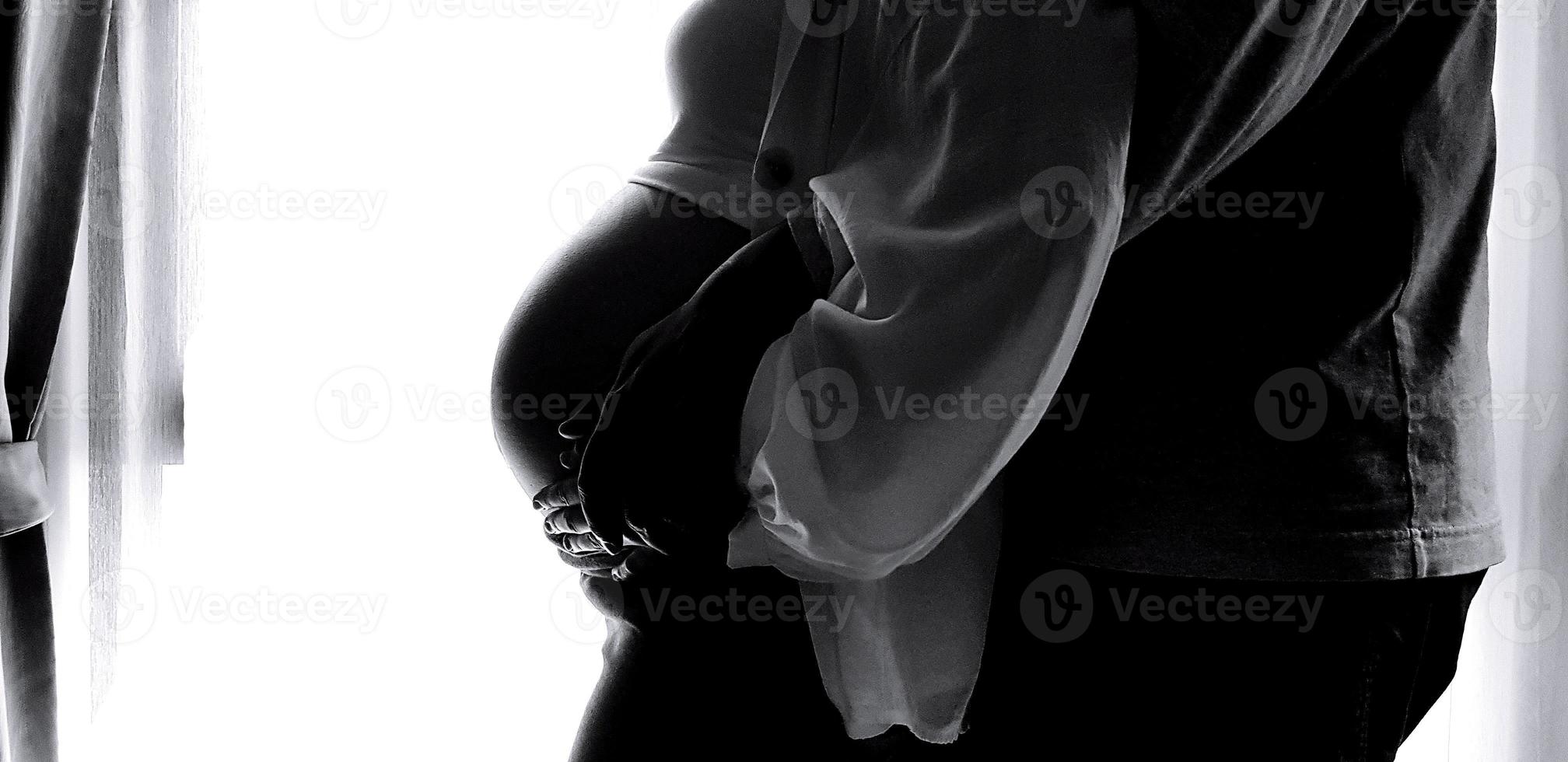 silhouette de proche en haut du mari main étreinte et émouvant femme ventre avec blanc rideau Contexte et la gauche copie espace dans noir et blanc Ton. enceinte, Nouveau la vie et amoureux famille dans monochrome style. photo