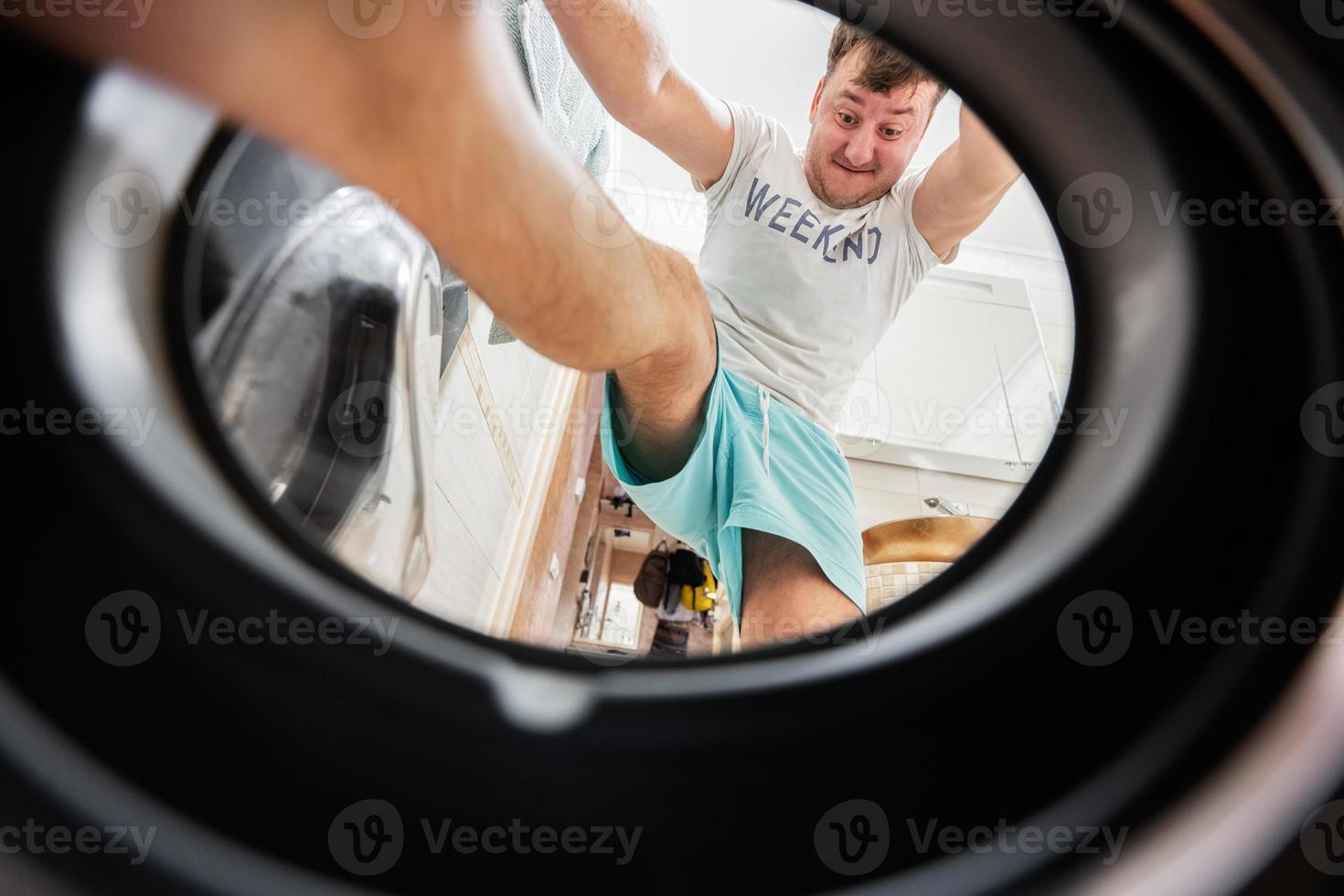 homme vue de la lessive machine à l'intérieur. Masculin Est-ce que du quotidien routine. grimpe à l'intérieur, pousser et pressage le blanchisserie avec le sien pieds. photo