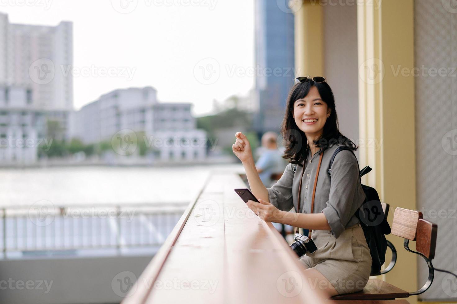 Jeune asiatique femme sac à dos voyageur en utilisant mobile téléphone dans Express bateau jetée sur chao Phraya rivière dans Bangkok. photo