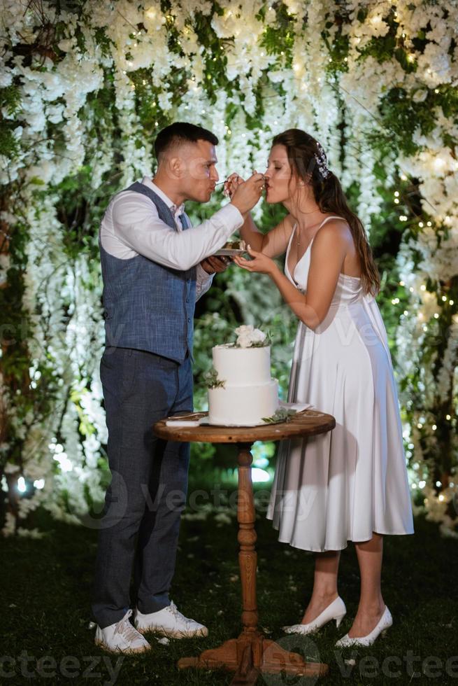 les jeunes mariés coupent et goûtent joyeusement le gâteau de mariage photo