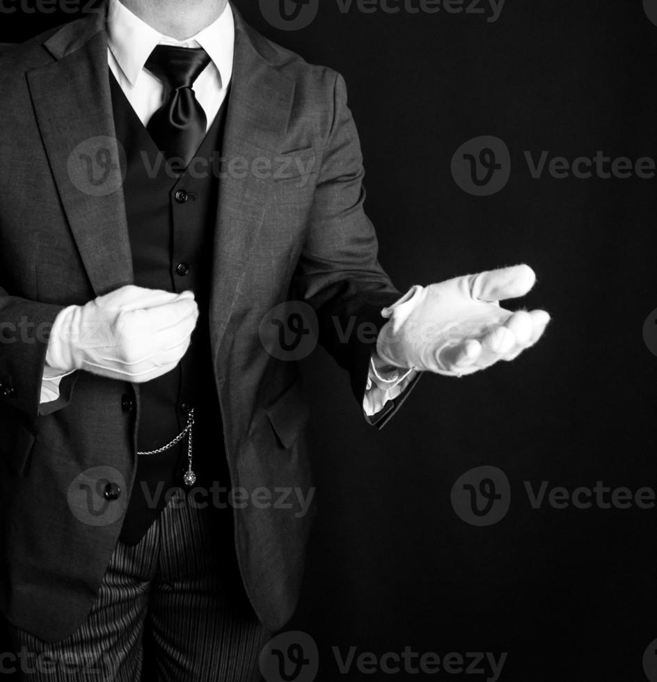 portrait de majordome dans foncé costume et blanc gants offre portion main. concept de un service industrie et professionnel courtoisie. photo