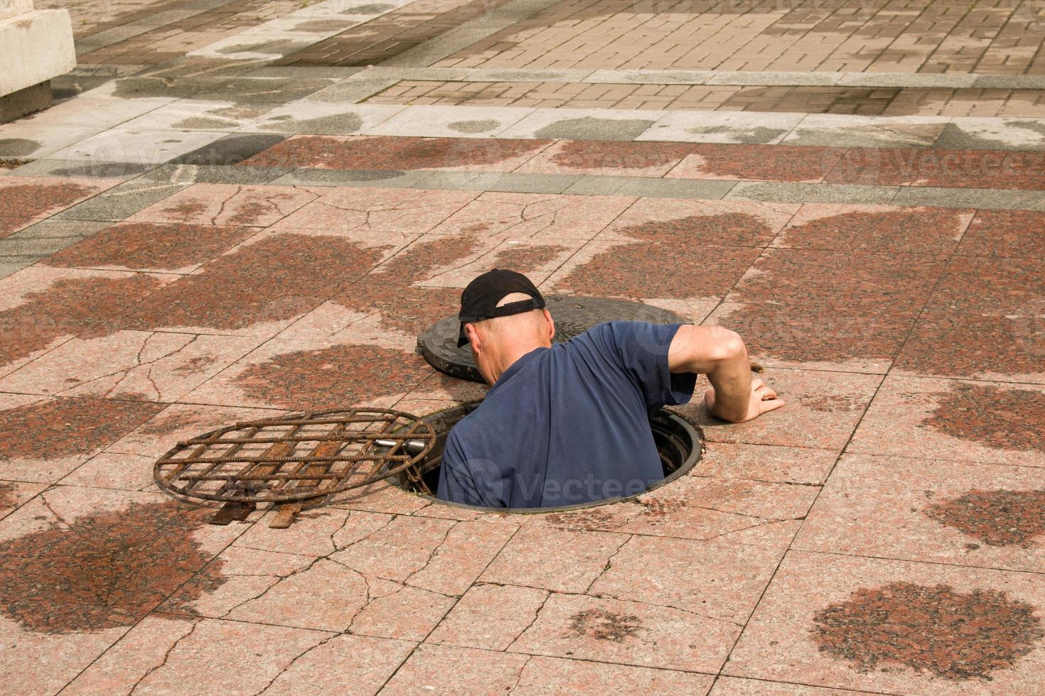 une ouvrier grimpe en dehors de un ouvert regard dans le route. dangereux ouvert non protégé regard sur le route. accident avec une égout regard dans le ville. le concept de réparer souterrain utilitaires. photo