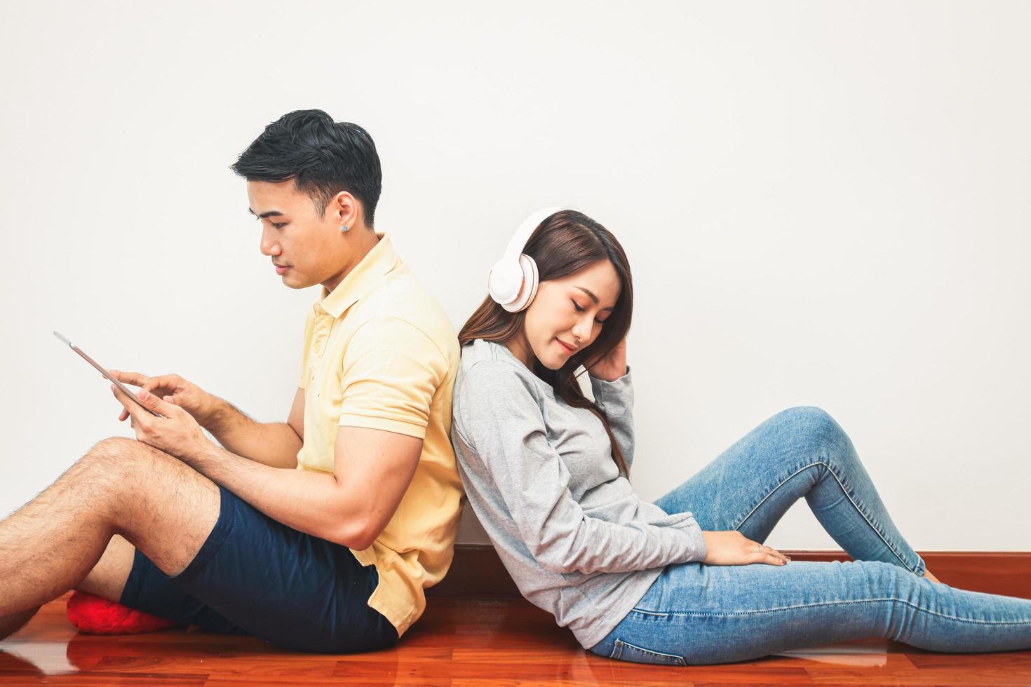 asiatique des couples asseoir retour contre chaque autre, Ecoutez à musique, et jouer le tablette. content à vivre ensemble dans le sien posséder maison. moderne famille concept photo