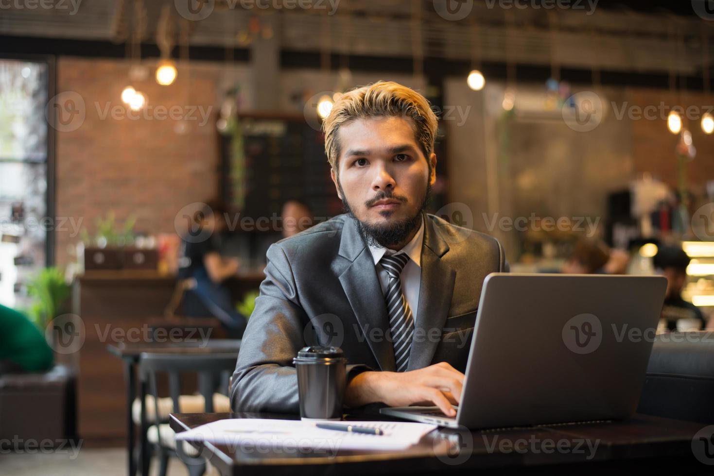 jeune homme d'affaires tenant une tasse de café tout en travaillant sur un ordinateur portable dans un café photo