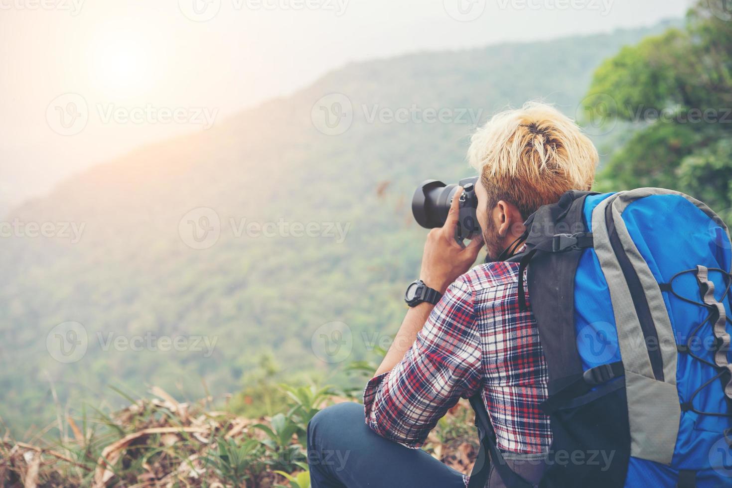 Arrière du jeune homme voyageur avec sac à dos debout sur la montagne et prendre une photo