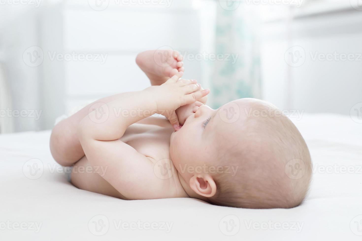 petite fille couchée et tirant sa jambe dans sa bouche photo