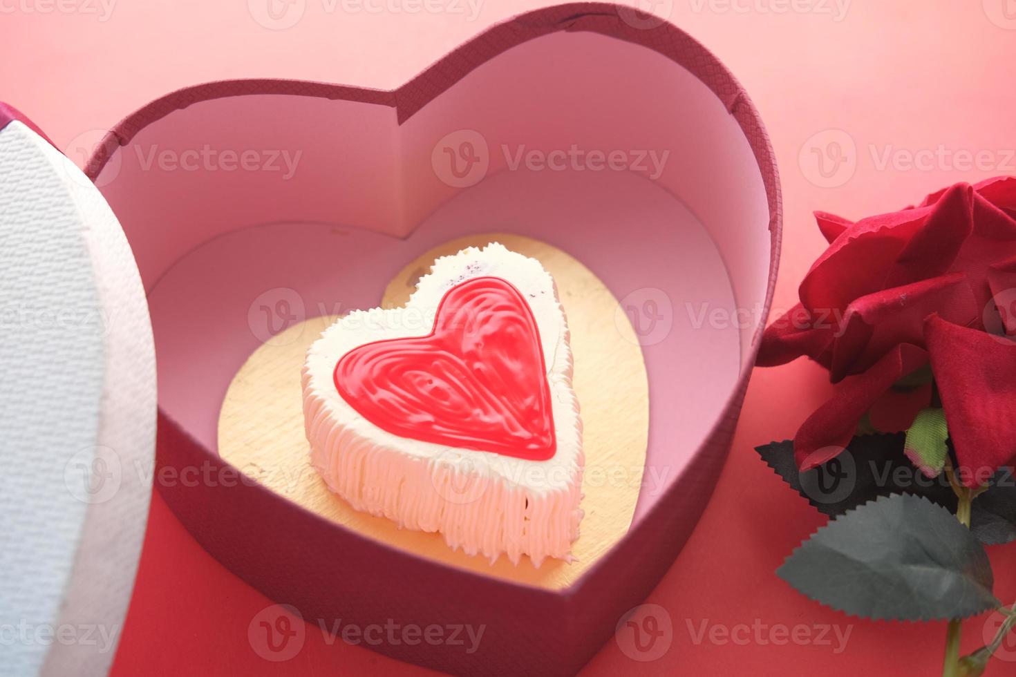 Vue de dessus du gâteau en forme de coeur, boîte-cadeau et fleur rose sur fond rouge photo