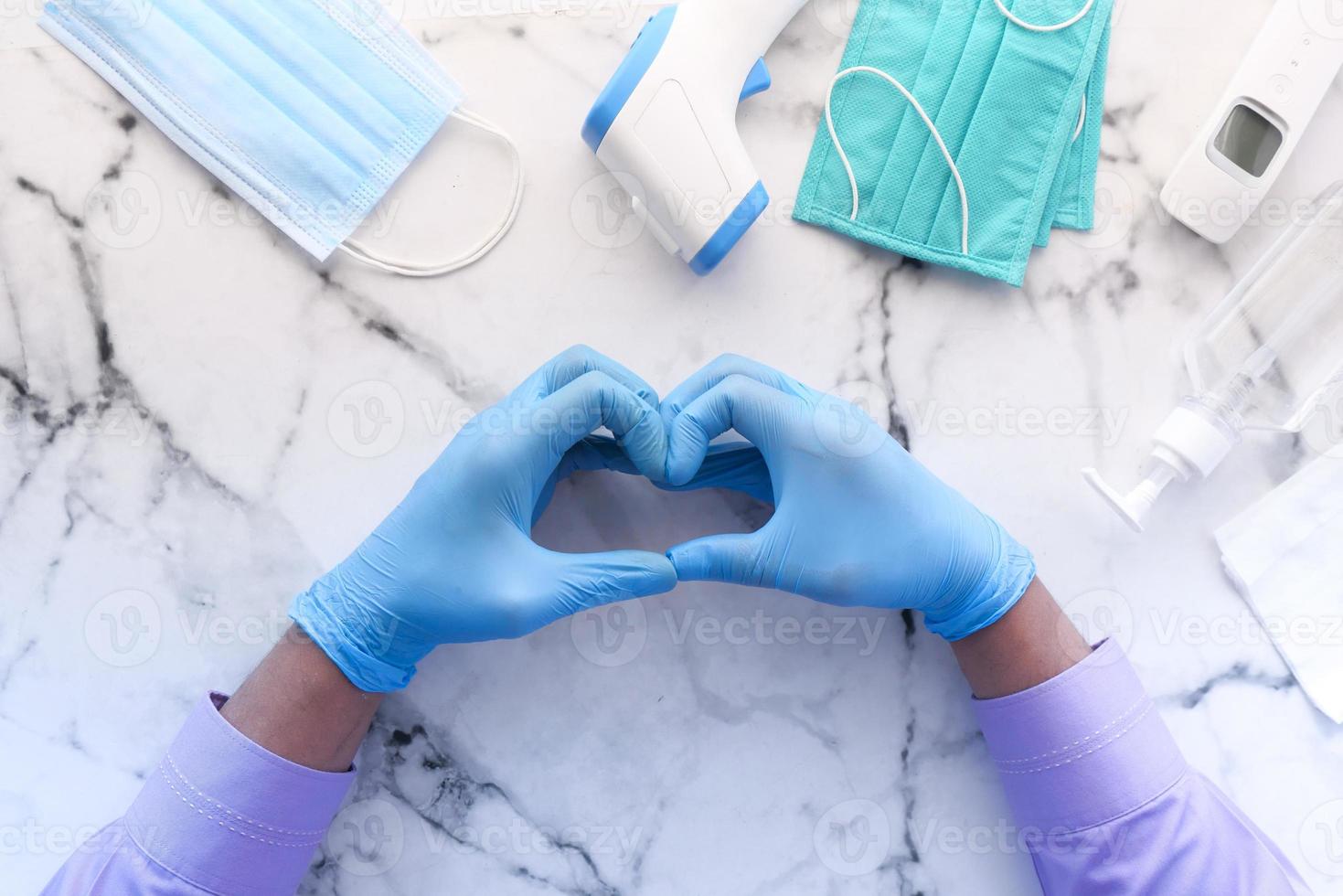 La main dans des gants en latex montrant le symbole en forme de coeur sur fond de carreaux photo