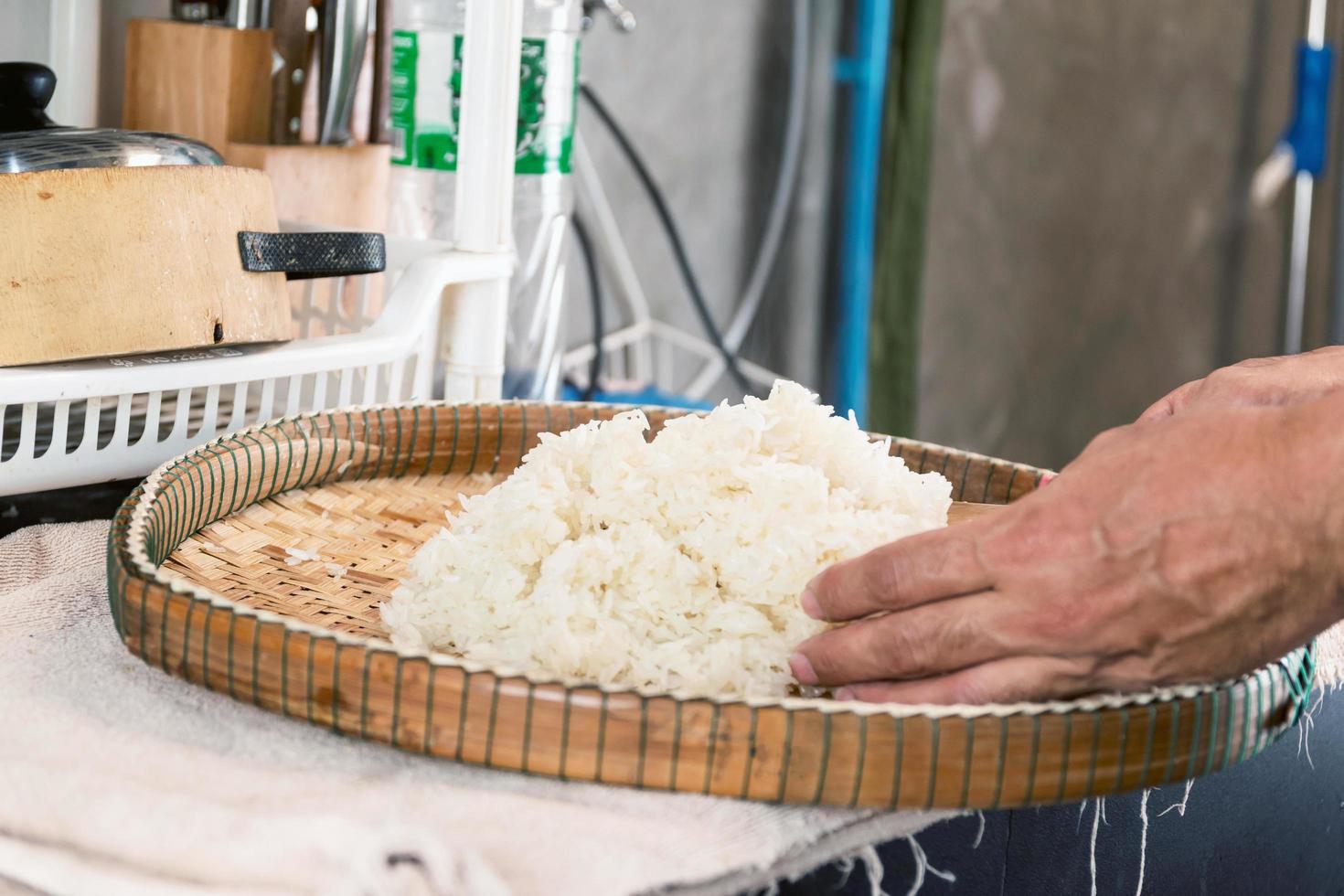 Mains plaçant du riz blanc cuit à la vapeur sur un plateau en bambou photo