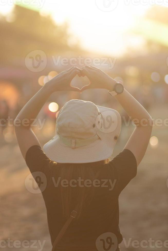 retour de femme avec sa mains élevé au dessus sa tête formes cœur symbole symbolisant l'amour la gentillesse et relation amicale avec magnifique sérénité contre Contexte de Matin lumière du soleil. concept de l'amour photo