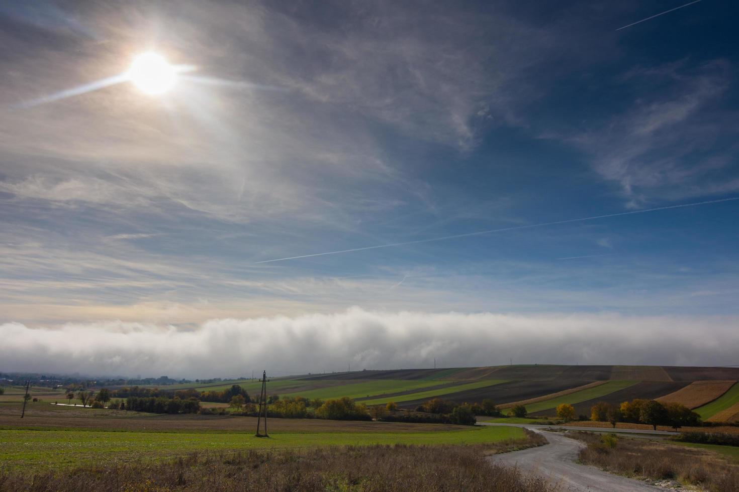 brillant Soleil sur bleu ciel plus de une blanc mur de dense brouillard sur le sol avec des champs photo