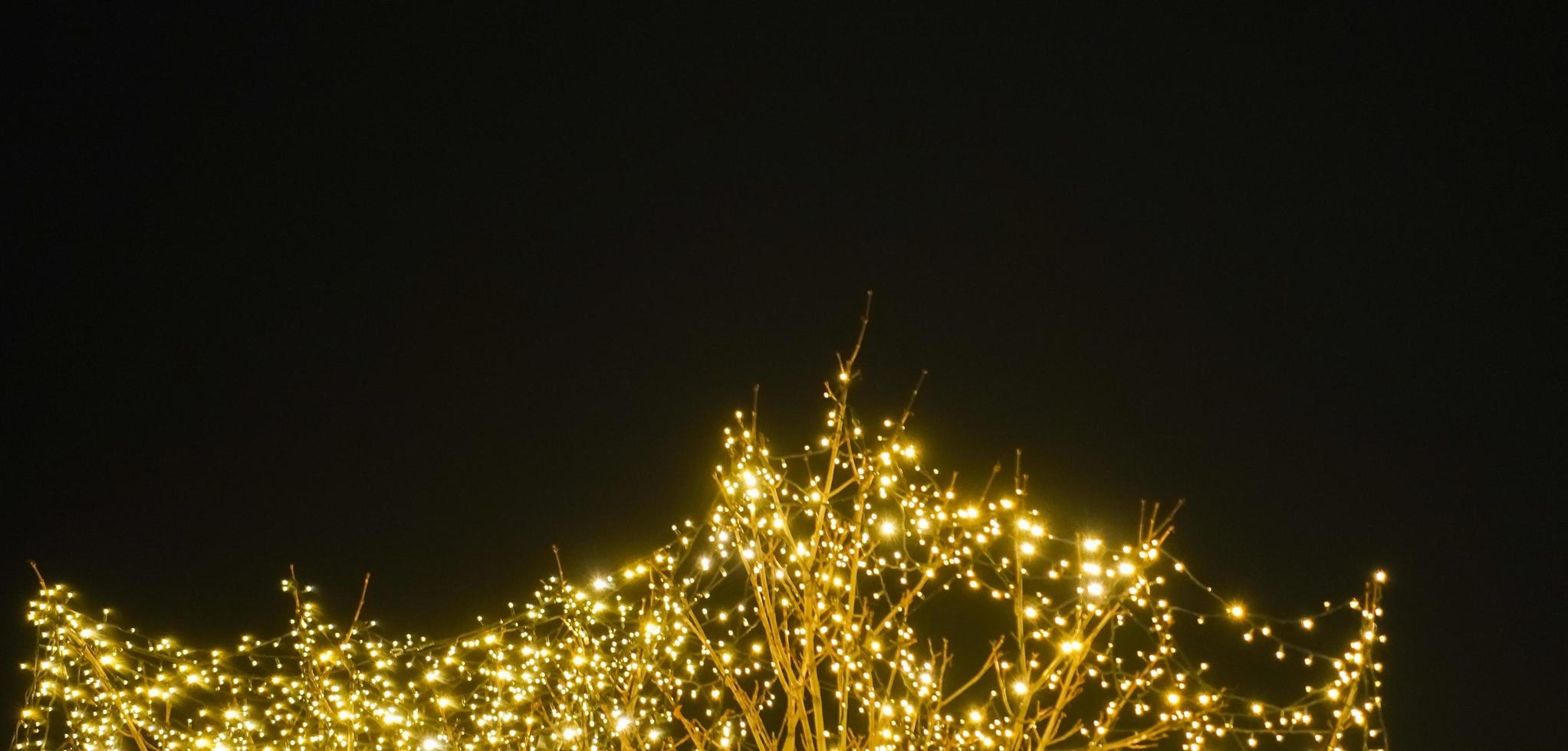 arbre avec beaucoup brillant lumières à une Noël marché avec noir ciel dans le Contexte panorama photo