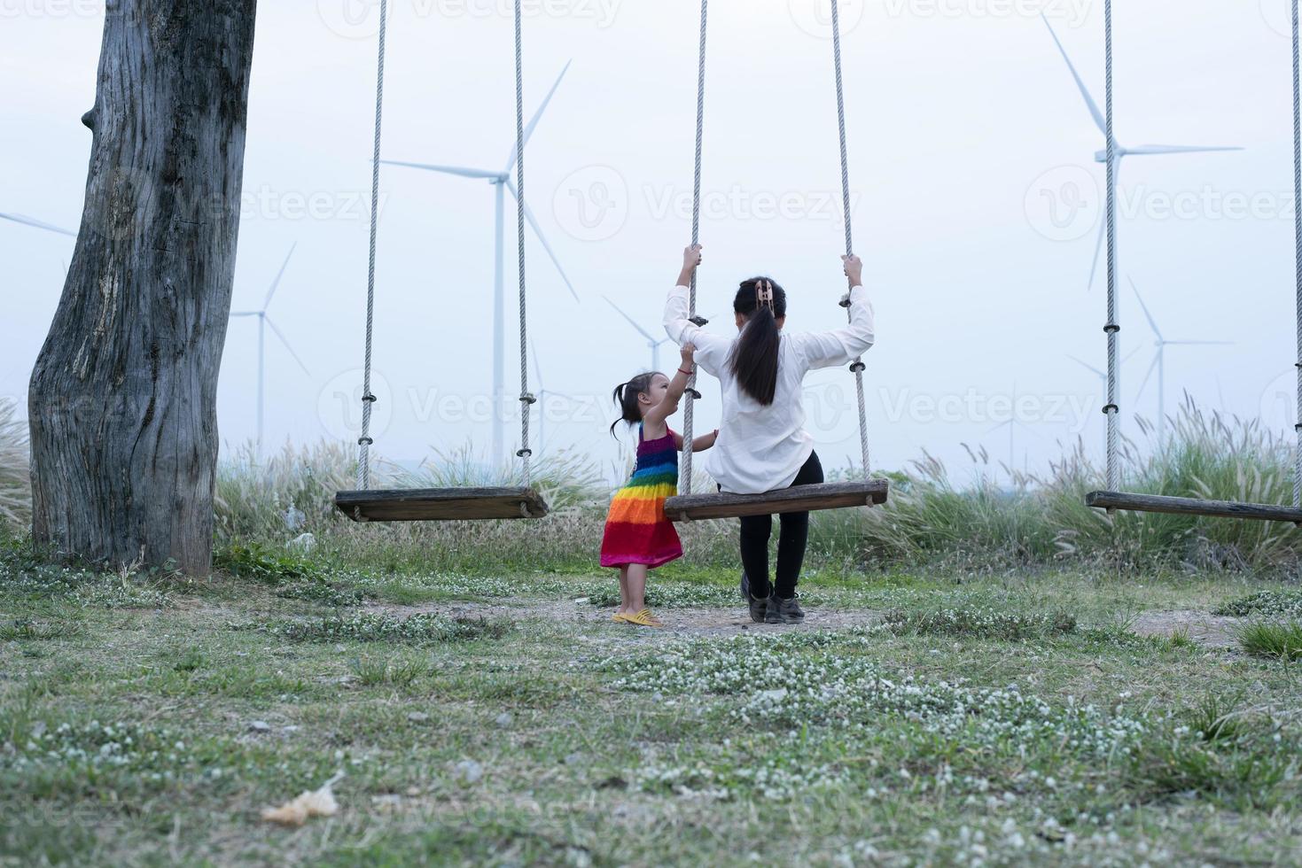 magnifique Jeune mère fille est assis et se détendre à été Prairie Contexte et Moulins à vent, Moulins à vent comme alternative énergie sources, durable Ressource concept, communauté gens avec Moulins à vent photo