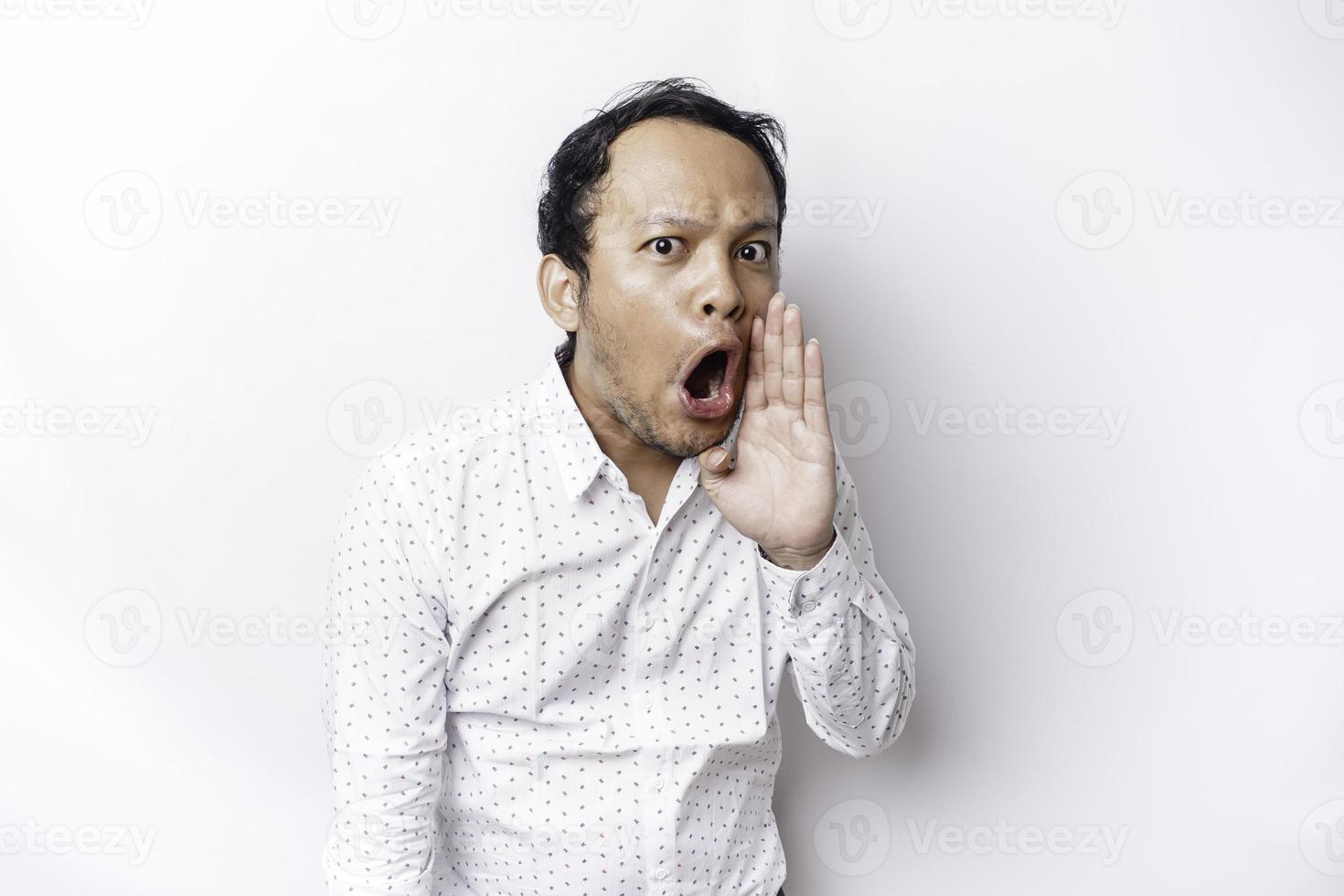 Jeune Beau homme portant une blanc chemise en criant et en hurlant bruyant avec une main sur le sien bouche. la communication concept. photo