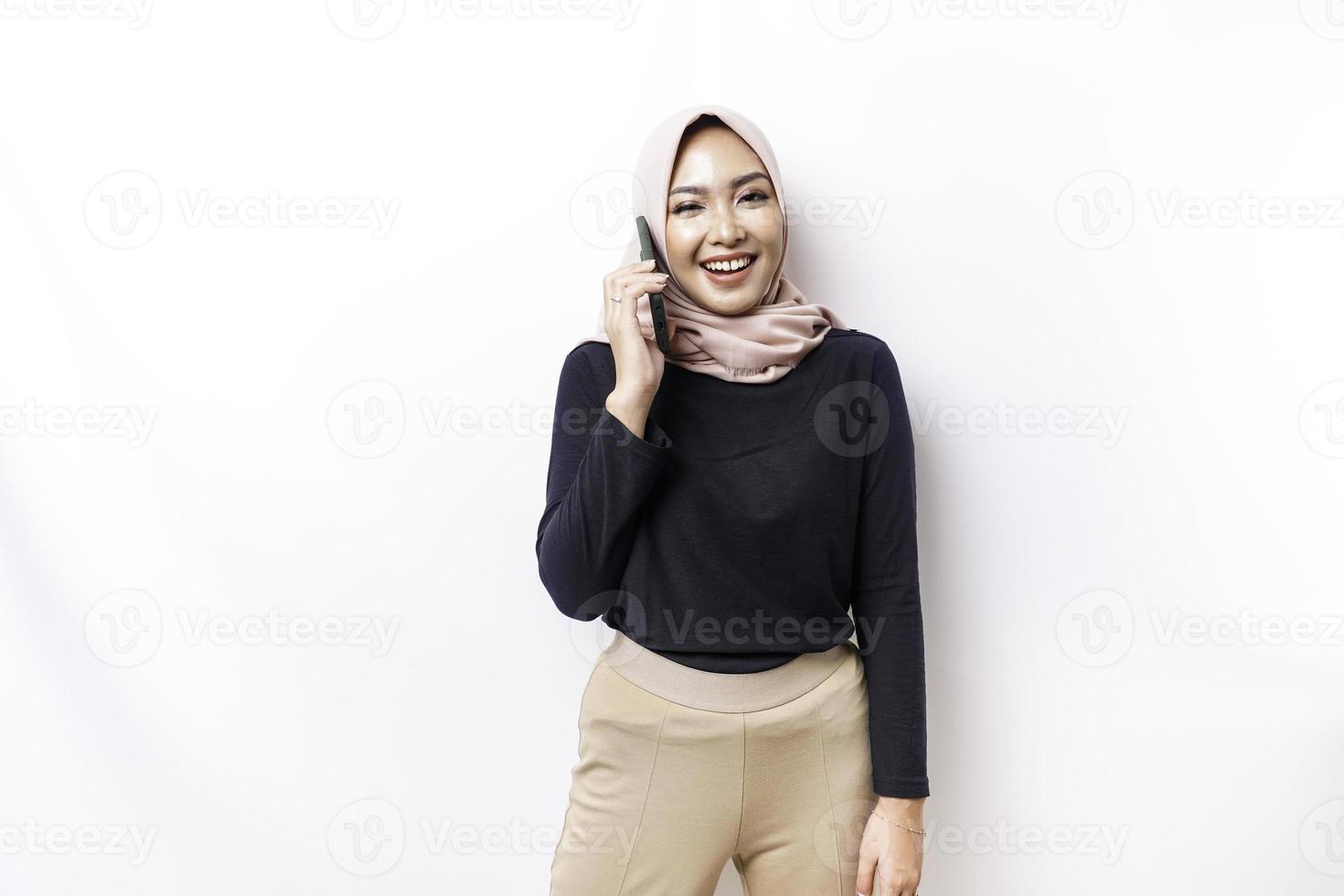 une portrait de une content asiatique musulman femme portant une hijab, en portant sa téléphone, isolé par blanc Contexte photo