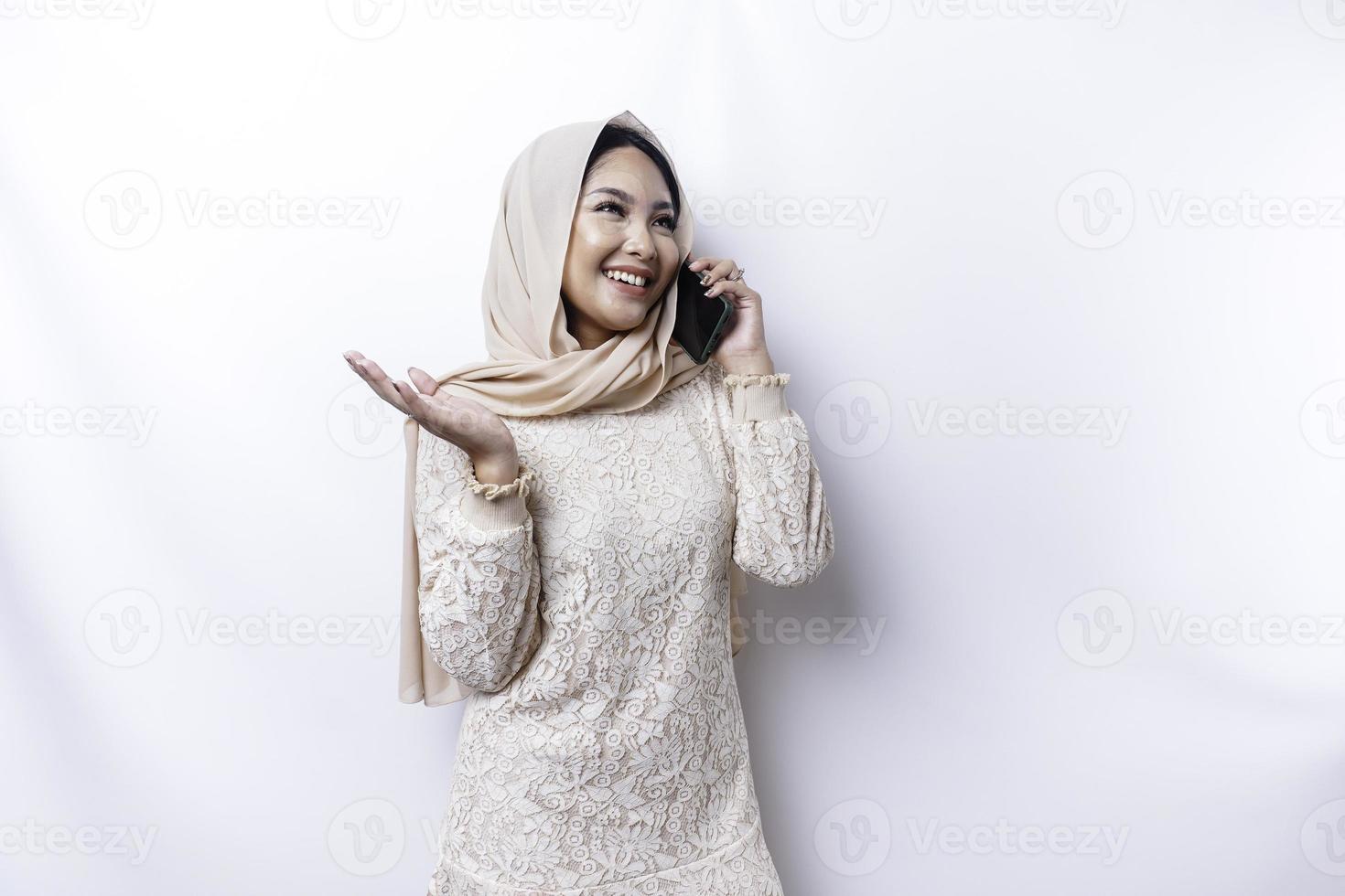 une portrait de une content asiatique musulman femme portant une hijab, en portant sa téléphone, isolé par blanc Contexte photo