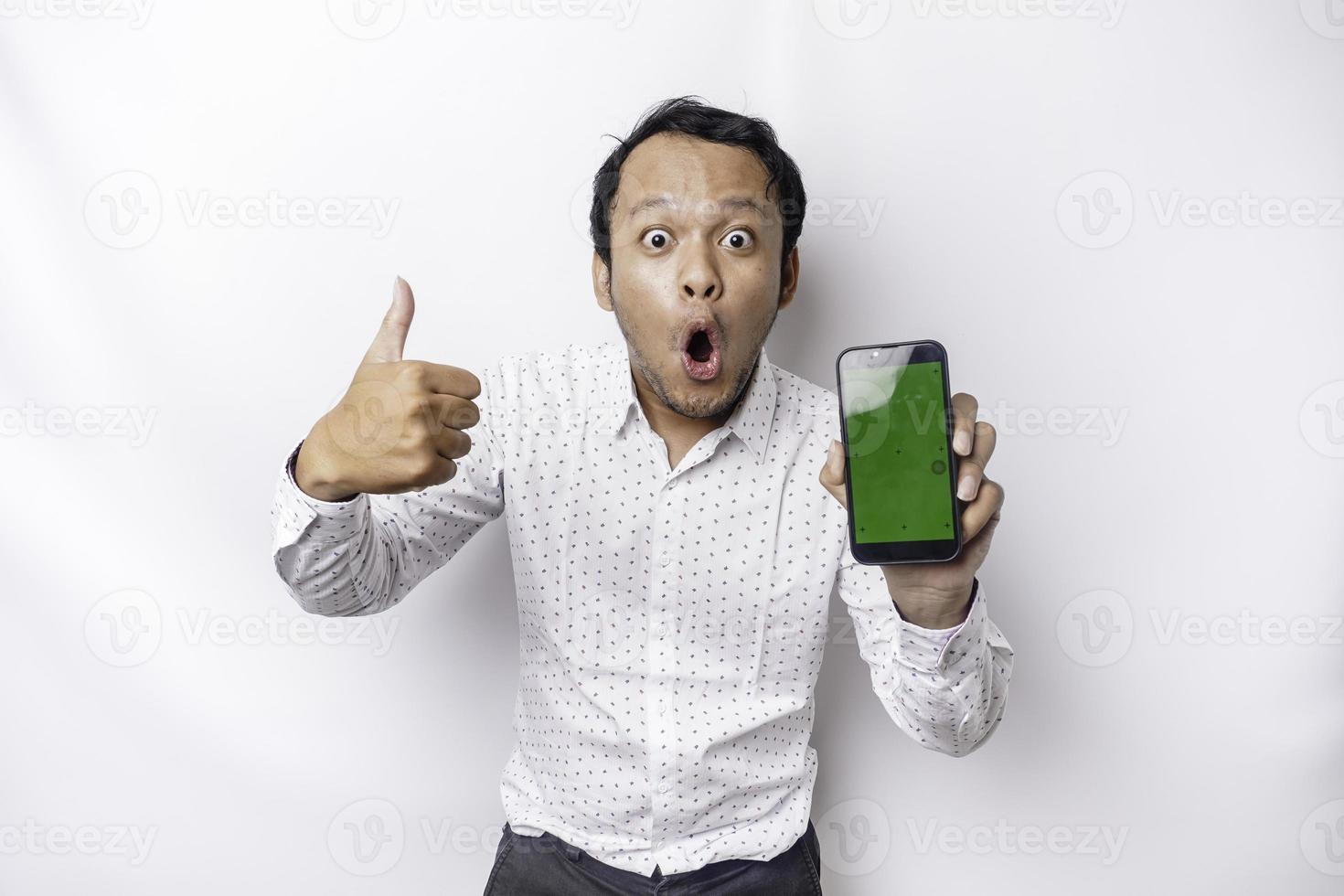 sous le choc asiatique homme portant une blanc chemise et montrant vert écran sur le sien téléphone, isolé par blanc Contexte photo