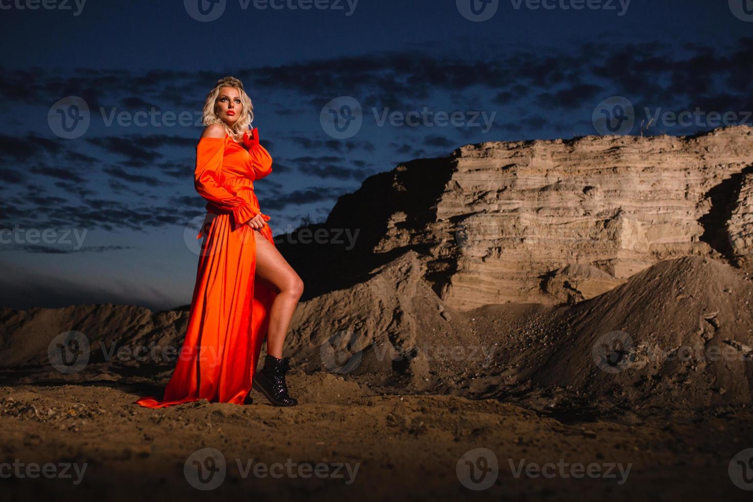 femme dans Orange robe avec svelte nu jambes posant près le le sable colline photo