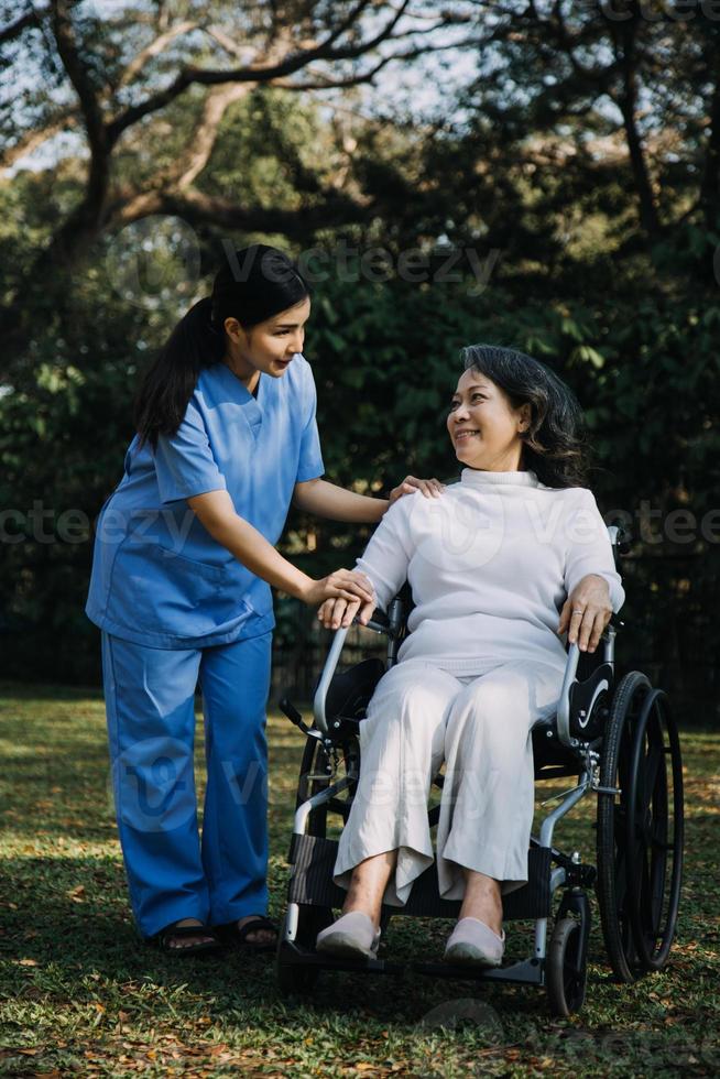 asiatique Jeune soignant infirmière soutien Sénior plus âgée Masculin en marchant en plein air. spécialiste fille médecin Aidez-moi et prendre se soucier de personnes âgées mature homme patient Faire physique thérapie dans Publique parc à allaitement maison. photo