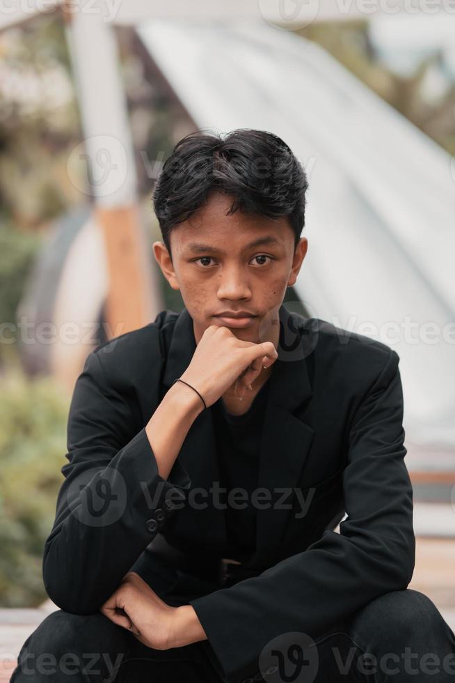 un asiatique adolescent dans une noir denim veste posant par séance sur une café chaise et relaxant photo