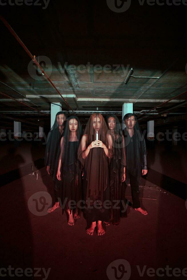 une groupe de diable fidèles dans tout noir vêtements et transparent voiles en portant bougies ensemble pendant une culte rituel dans une bâtiment photo
