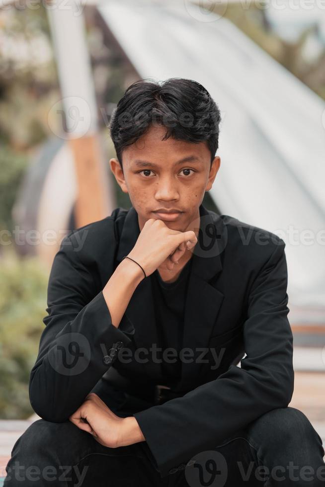 un asiatique adolescent dans une noir denim veste posant par séance sur une café chaise et relaxant photo