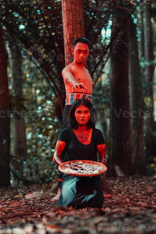 un asiatique femme et homme étaient permanent dans de face de une arbre tandis que chasse un animal dans le milieu de le forêt jusqu'à ce que elles ou ils étaient couvert dans du sang photo