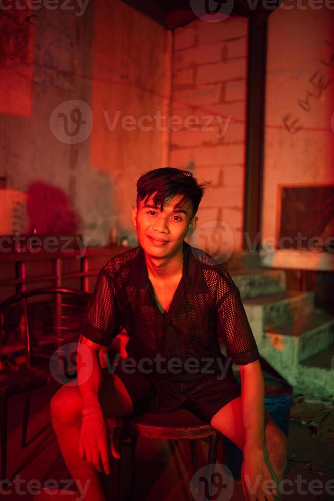 une gay homme portant noir et posant avec une chaise dans un vieux maison avec une rouge lumière photo