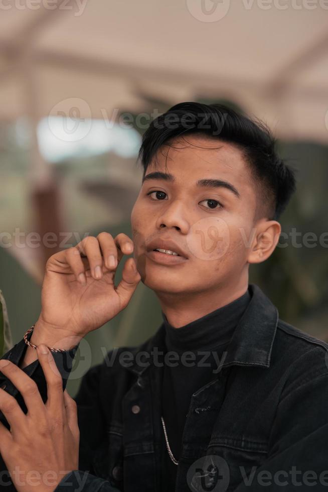 un asiatique homme dans une noir denim veste posant avec une de bonne humeur visage et très Beau dans une café photo