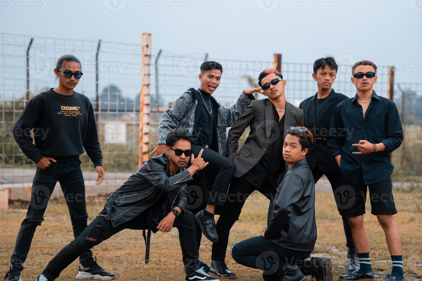 une groupe de adolescent garçons dans noir vêtements posant très galamment avec leur copains dans une champ photo